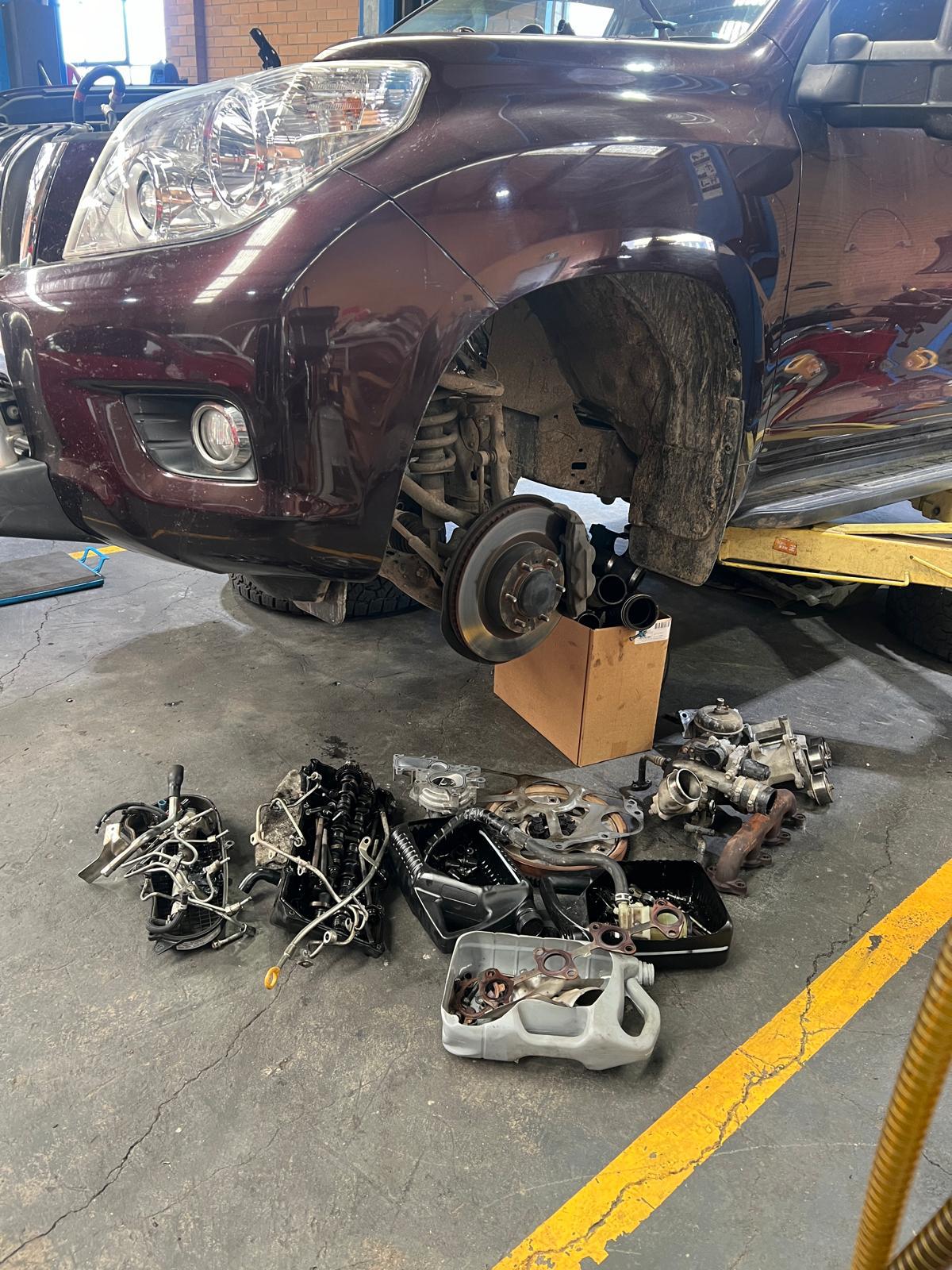 4WD on the hoist with its front wheel off and engine parts laid out on the floor