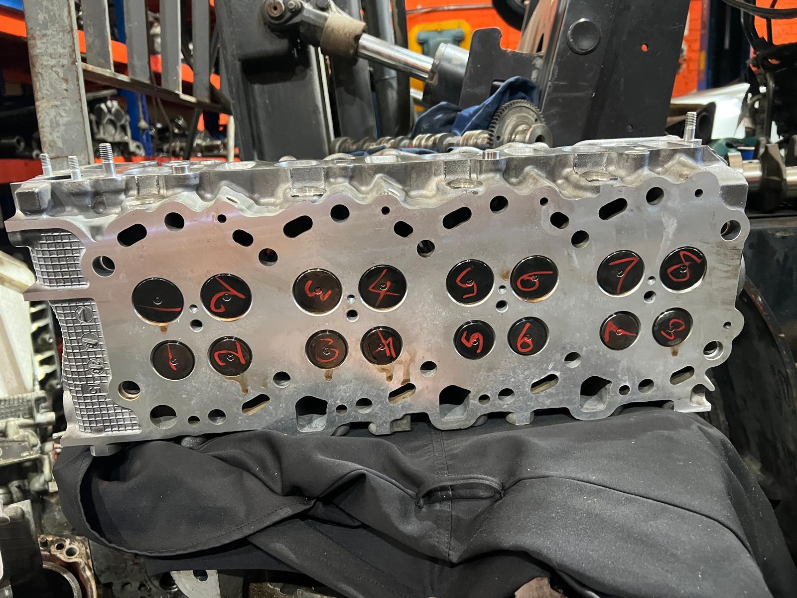 Diesel cylinder head with valves numbered in red marker, ready for reassembly